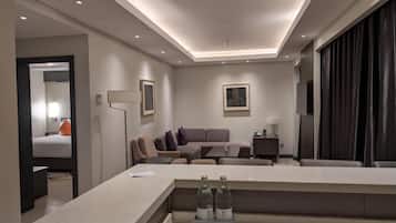 A modern hotel room with a sofa, a coffee table, a TV, and a minibar.
