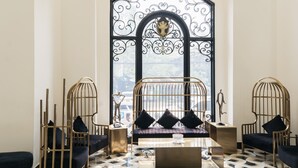 A room with a large arched window, a central sofa with black cushions, and two side chairs with black cushions.