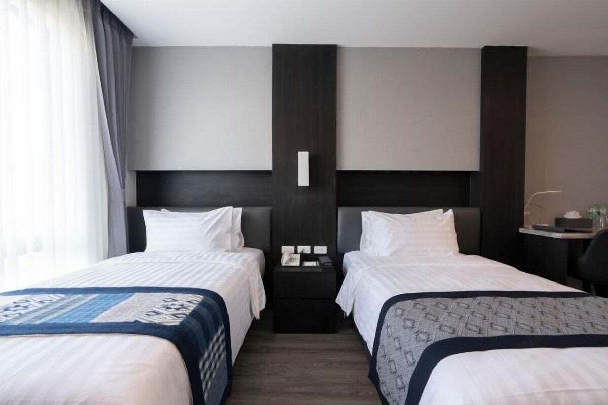 Habitación de hotel con dos camas, una mesita de noche y un escritorio con silla.