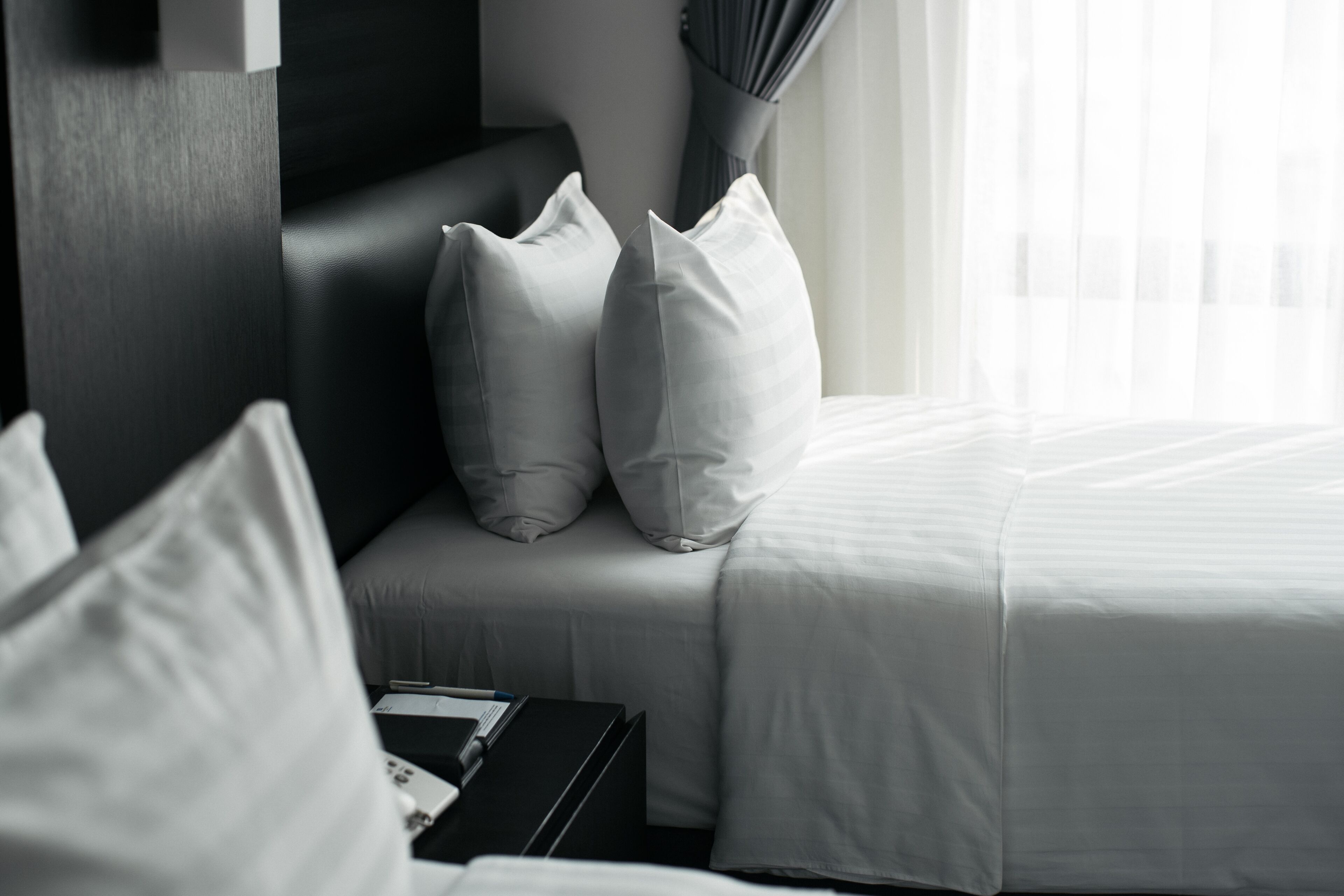 A hotel room with a bed, pillows, a nightstand, and a vase of flowers.