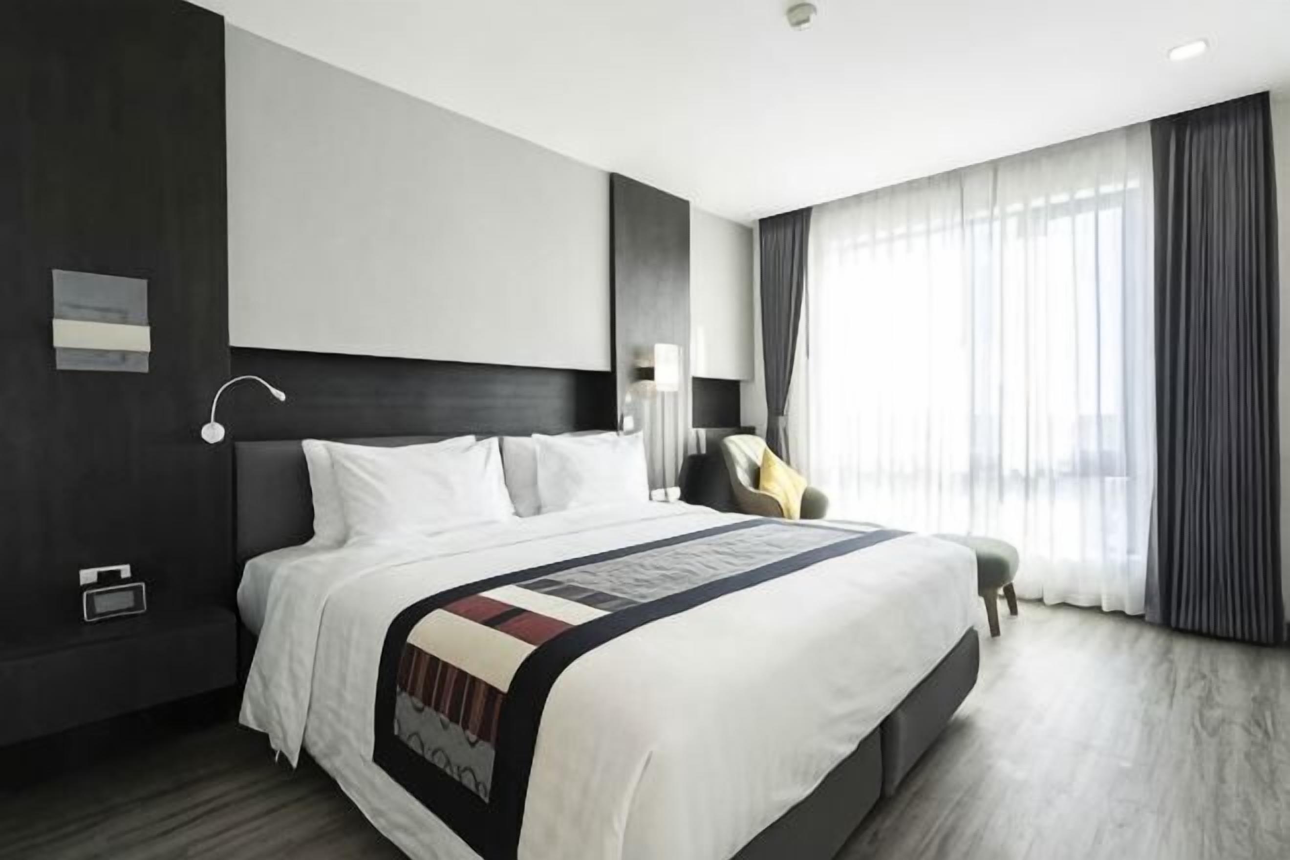 Et moderne hotelværelse med en stor seng, et sengebord, en stol og et vindue med gardiner.