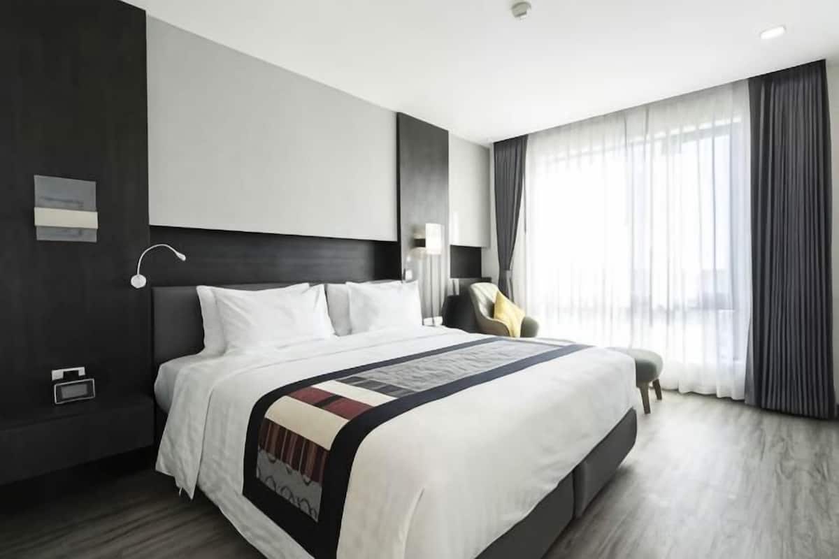A modern hotel room with a large bed, a bedside table, a chair, and a window with curtains.