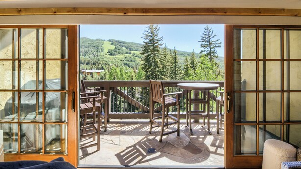 Une chambre avec balcon, des meubles en bois et une vue sur un paysage boisé.