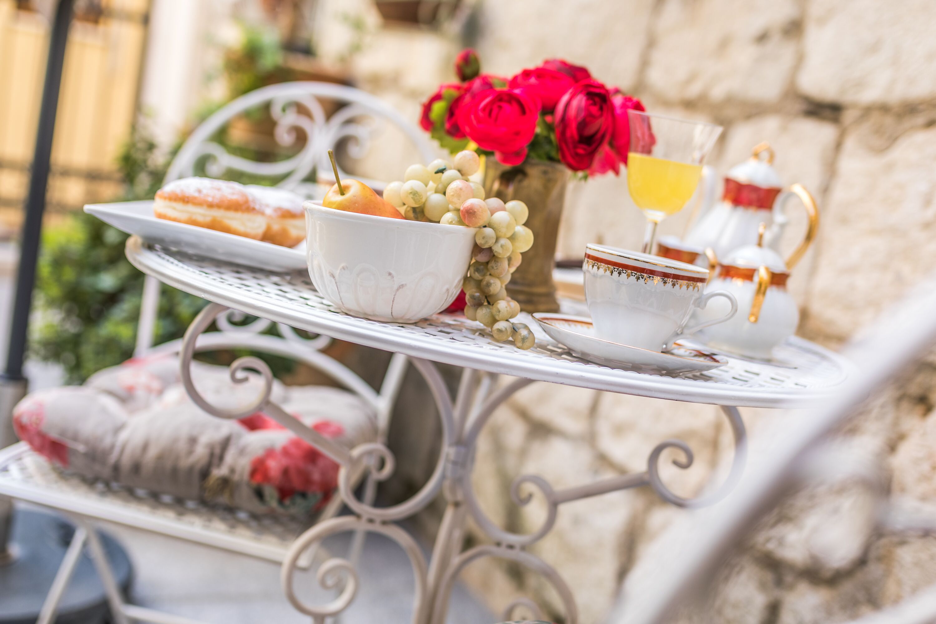 A table set with pastries, a bowl of fruit, a vase of flowers, and a teapot.
