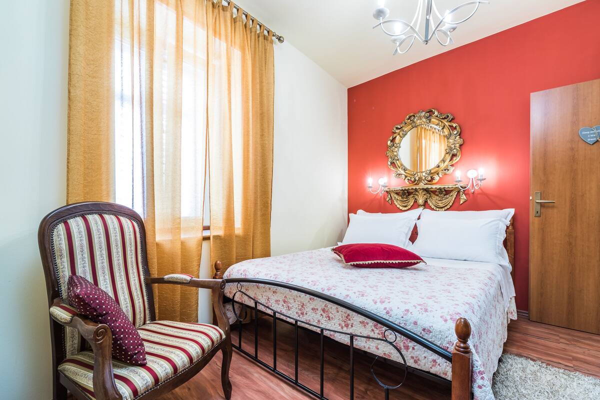 Een slaapkamer met een bed, een stoel, een spiegel en een deur.
