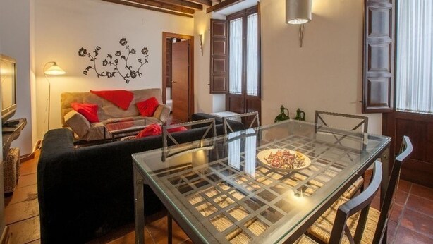 Ein gemütliches Wohnzimmer mit Glastisch, Holzbalken an der Decke, einer Couch mit roten Kissen und einem Wandbild.