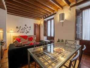 Un salon chaleureux avec une table à plateau en verre, des poutres en bois au plafond, un canapé avec des coussins rouges et une œuvre d’art murale.