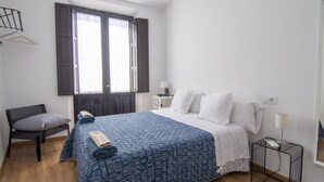 Ein Schlafzimmer mit einem Bett, einem Sessel, einem Nachttisch und einem Fenster mit Vorhängen.