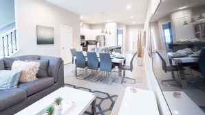 Un salon moderne avec un canapé, une table basse, un coin repas avec des chaises et une cuisine en arrière-plan.