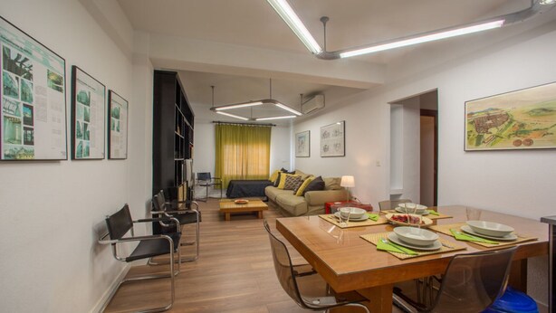 Una sala de estar moderna con comedor, que presenta una mesa de madera para cuatro personas, un sofá y una estantería.