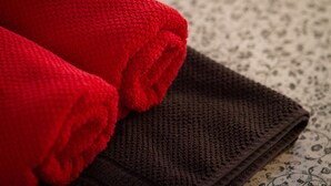 Dos toallas enrolladas, una roja y otra marrón, sobre una superficie estampada.