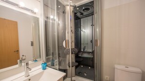 Un baño moderno con ducha de vidrio, lavamanos blanco con espejo y retrete.