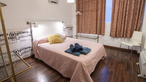 Un dormitorio ordenado con cama, mesita de noche, lámpara colgante, ventana con cortinas y aire acondicionado de pared.