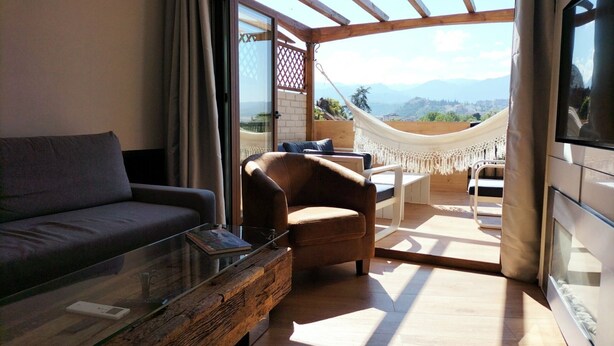 A modern living room with a sofa, armchair, and glass coffee table. A hammock and outdoor seating are visible through an open door. - Realejo Paradise. Penthouse with terrace (Granada)