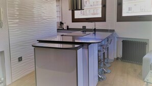 A modern kitchen with a central island, bar stools, a window with a view, and a built-in stove. - Realejo Paradise. Penthouse with terrace (Granada)