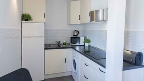 Une cuisine compacte avec des meubles blancs, une hotte de cuisinière en acier inoxydable, un four à micro-ondes, un lave-linge et un grille-pain.