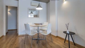 Un coin repas comprenant une table ronde, quatre chaises blanches, un luminaire suspendu et une petite table d’appoint sur laquelle est posé un vase.