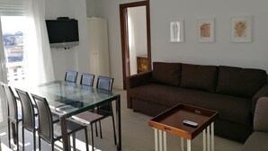 Ein modernes Wohnzimmer mit einem Glastisch, einem braunen Sofa und einem an der Wand montierten Fernseher.