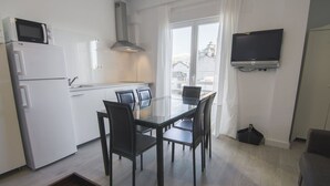 Eine moderne Küche mit weißen Geräten, einem Esstisch mit Stühlen und einem flachbildfernseher an der Wand.