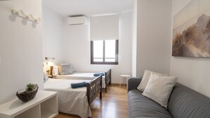 Una habitación minimalista con una cama, un sofá, una mesita pequeña y un aire acondicionado de pared.