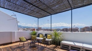 Una terraza en la azotea con mobiliario exterior, una pérgola y vistas de la ciudad.