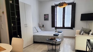 Una habitación pequeña con cama, mesita de noche y una pequeña mesa redonda con una cesta.