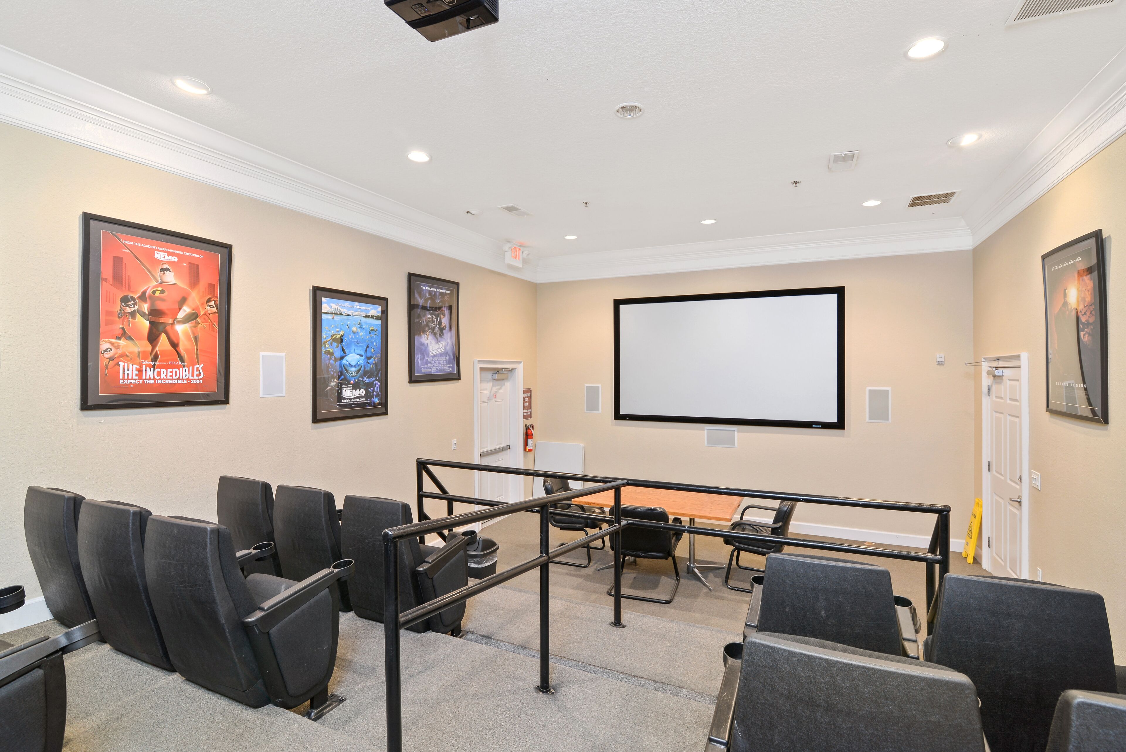 A conference room with a large screen, black chairs, and framed movie posters on the walls.