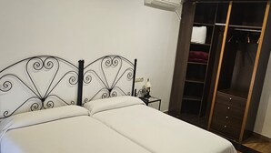 A room with two beds, a wooden floor, a wardrobe, and an air conditioning unit. - Hostal El Pasaje (Puente Genil)