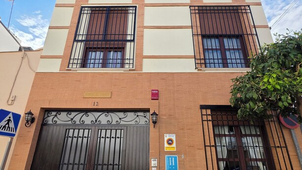 A two-story building with a large entrance gate, potted plants, and a sign indicating a fire exit. - Hostal El Pasaje (Puente Genil)