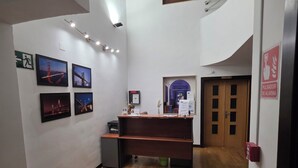 A reception area with a wooden desk, a fire extinguisher, and framed pictures on the wall. - Hostal El Pasaje (Puente Genil)