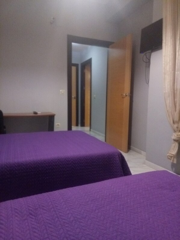 A room with two beds, a desk, a TV, and a door leading to another room.