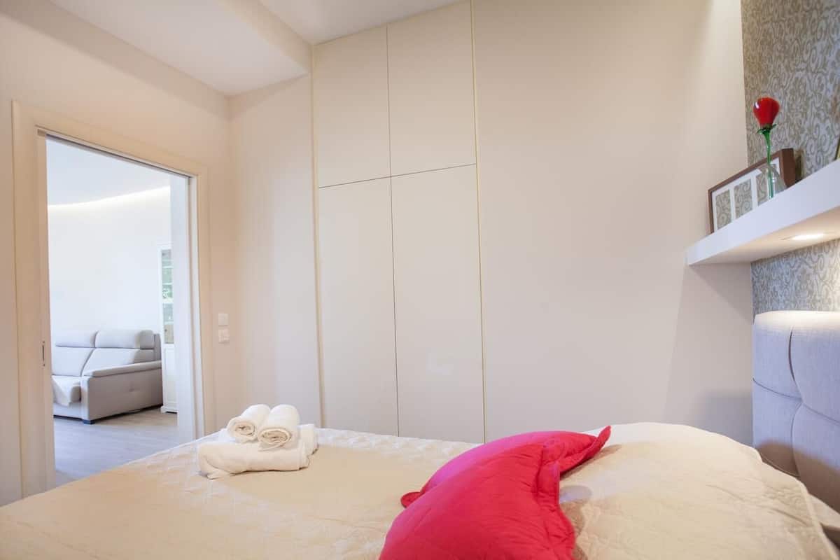Un dormitorio con una cama, una almohada roja y un juego de toallas.