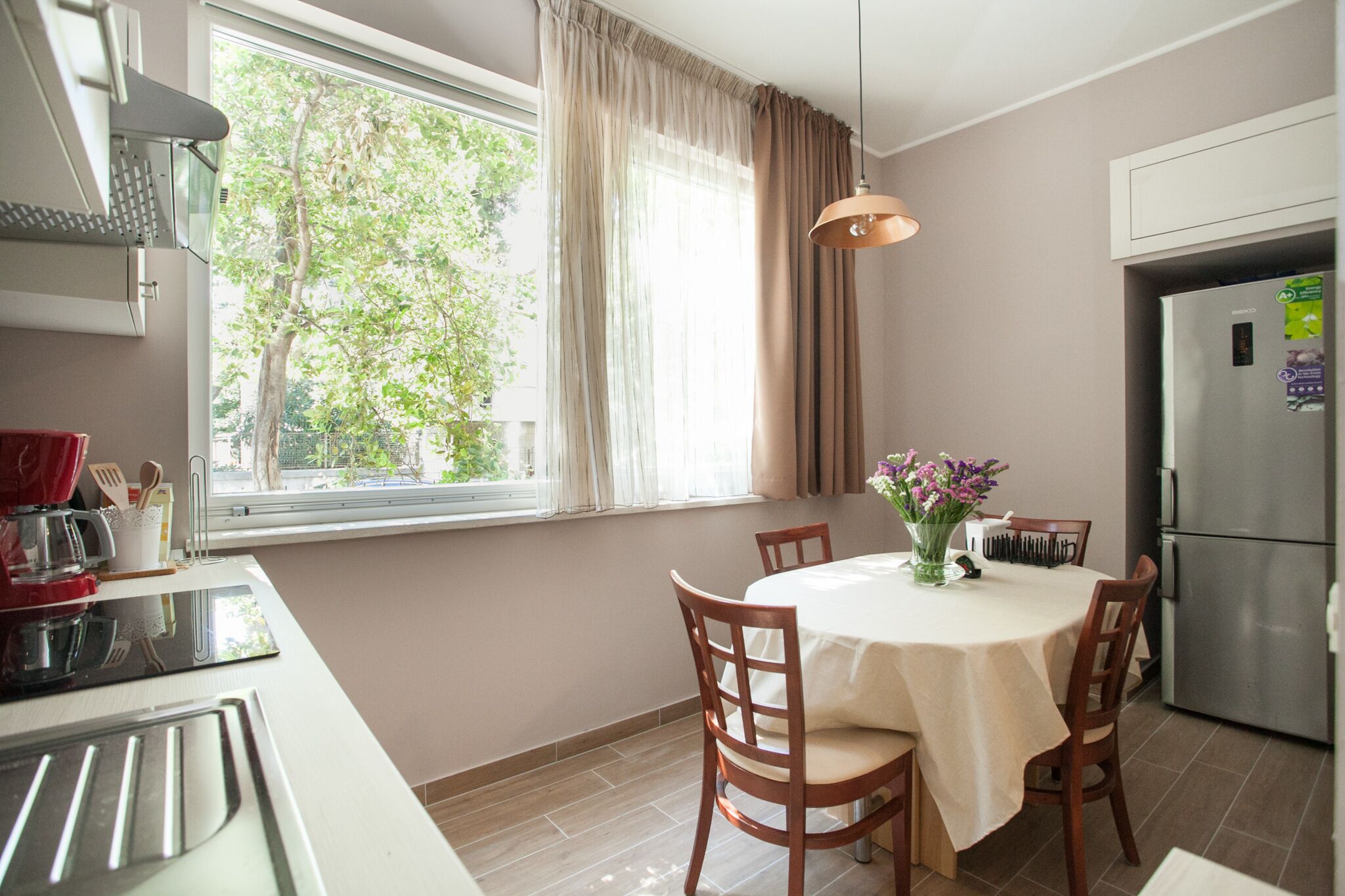 A modern kitchen with a dining area, large window, and stainless steel appliances.