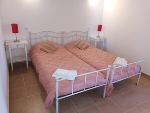 Un lit double avec une couette rose, deux tables de chevet avec des lampes rouges et une tête de lit blanche.