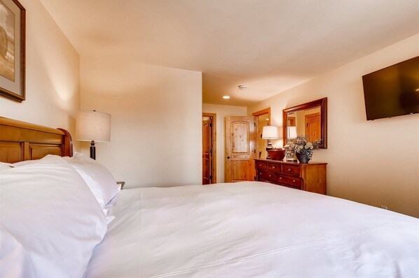 A hotel room with a large bed, a wooden dresser, a mirror, and a framed picture on the wall. - Villa Cortina in Vail Village! New Pool, Walk to the Lifts, Shops, Restaurants, and Nightlife! (Vail)