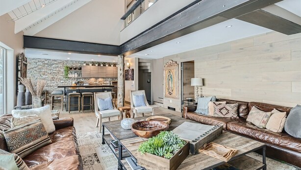 A spacious living room with a high ceiling, a stone wall, and a kitchen in the background. - 970-B Fairway Ct., Vail Golf Course Home - Hot Tub, Fire Pit,Gas Grill, Close to Lifts! (Vail)