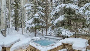 A hot tub surrounded by snow-covered trees and a stone wall. - 970-B Fairway Ct., Vail Golf Course Home - Hot Tub, Fire Pit,Gas Grill, Close to Lifts! (Vail)