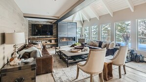 A spacious living room with a fireplace, comfortable seating, and large windows offering a view of the outdoors. - 970-B Fairway Ct., Vail Golf Course Home - Hot Tub, Fire Pit,Gas Grill, Close to Lifts! (Vail)