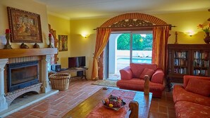 A living room with a fireplace, a sofa, a television, and a bookshelf. - Gorgeous villa ideally located with pool, ocean views, AirCo, great for families (Carvoeiro)