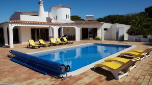 A swimming pool with sun loungers and a covered area, surrounded by a white building with a tiled roof. - Gorgeous villa ideally located with pool, ocean views, AirCo, great for families (Carvoeiro)