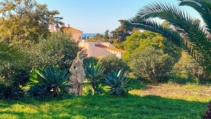 A garden with a statue, lush greenery, and a building in the background. - Gorgeous villa ideally located with pool, ocean views, AirCo, great for families (Carvoeiro)