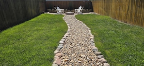 A backyard with a gravel path, two white chairs, and a wooden fence.