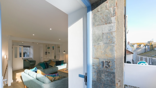 Una sala de estar moderna con un sofá, sillas y una mesa de centro. Se ve una puerta con un muro de piedra y un número.