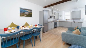 Una cocina moderna con armarios grises, un refrigerador de acero inoxidable y una zona de comedor con sillas azules y una mesa lista para el desayuno.
