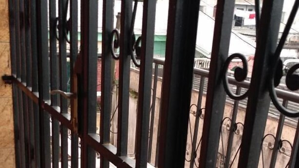 Una reja de metal con barras verticales y detalles decorativos, que da acceso a un espacio al aire libre.