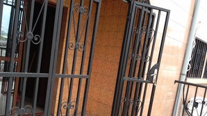 Una reja metálica con diseños intrincados, que da acceso a la entrada de un edificio con un muro de azulejos.