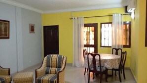 Un salón con pared amarilla, una mesa de comedor con sillas, un sofá y una mesita.