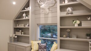 A cozy reading nook with a built-in bench, shelves with decorative items, and a large window with a view of trees.
