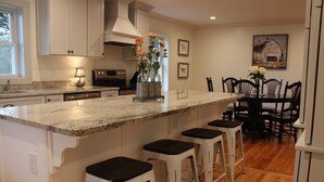 A kitchen with a large island, bar stools, a dining table with chairs, and a painting on the wall.
