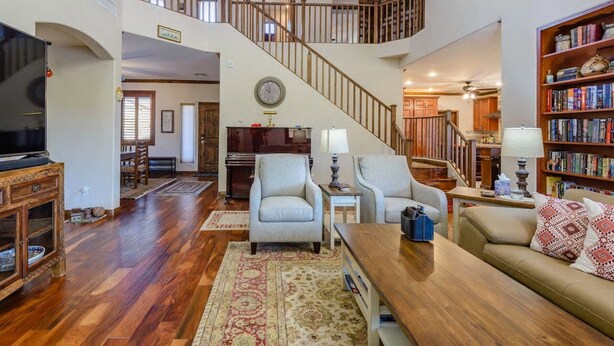 A spacious living area with a wooden staircase, a television, a bookshelf, and a dining area. - Relax in Home w/ Htd. Pool+Hot Tub,  Putting Green, Whirlpool Bath+Steam Shower (Queen Creek)